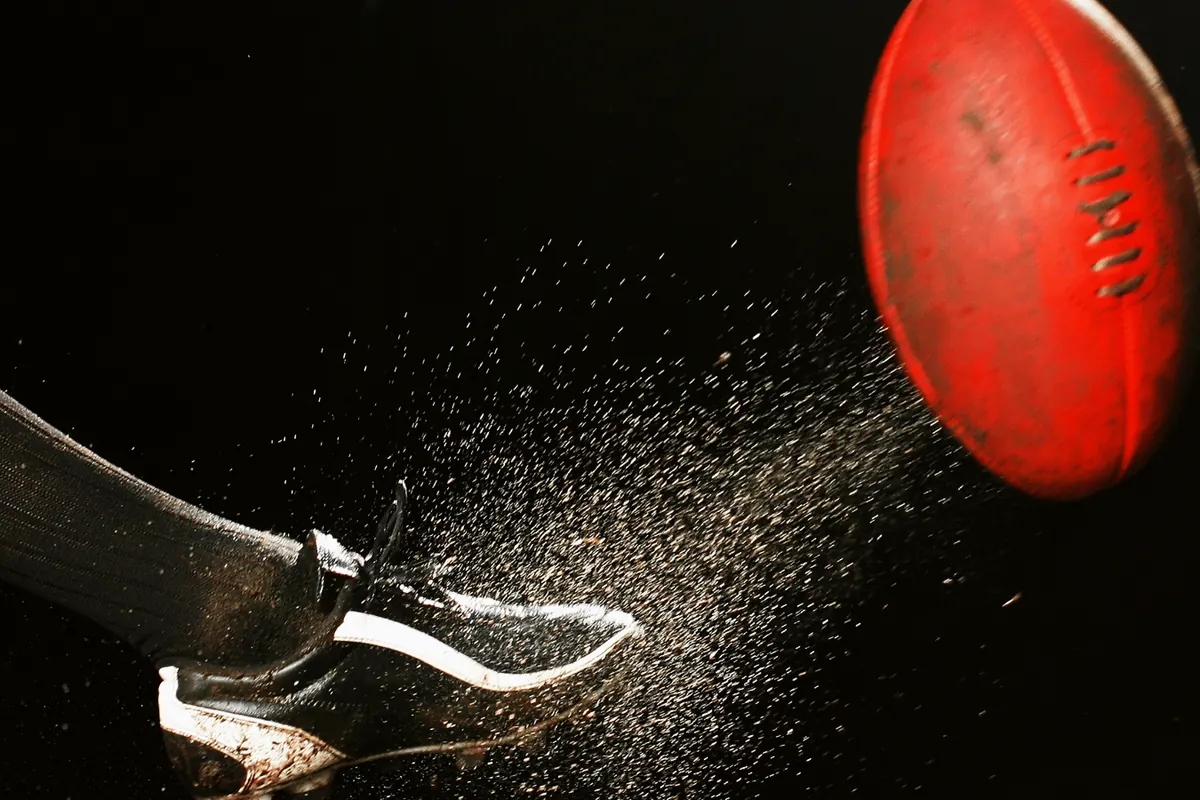 A boot striking a football, dust flying, against a black background