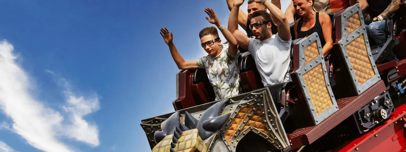 Riders with their arms up on a rollercoaster against a blue sky