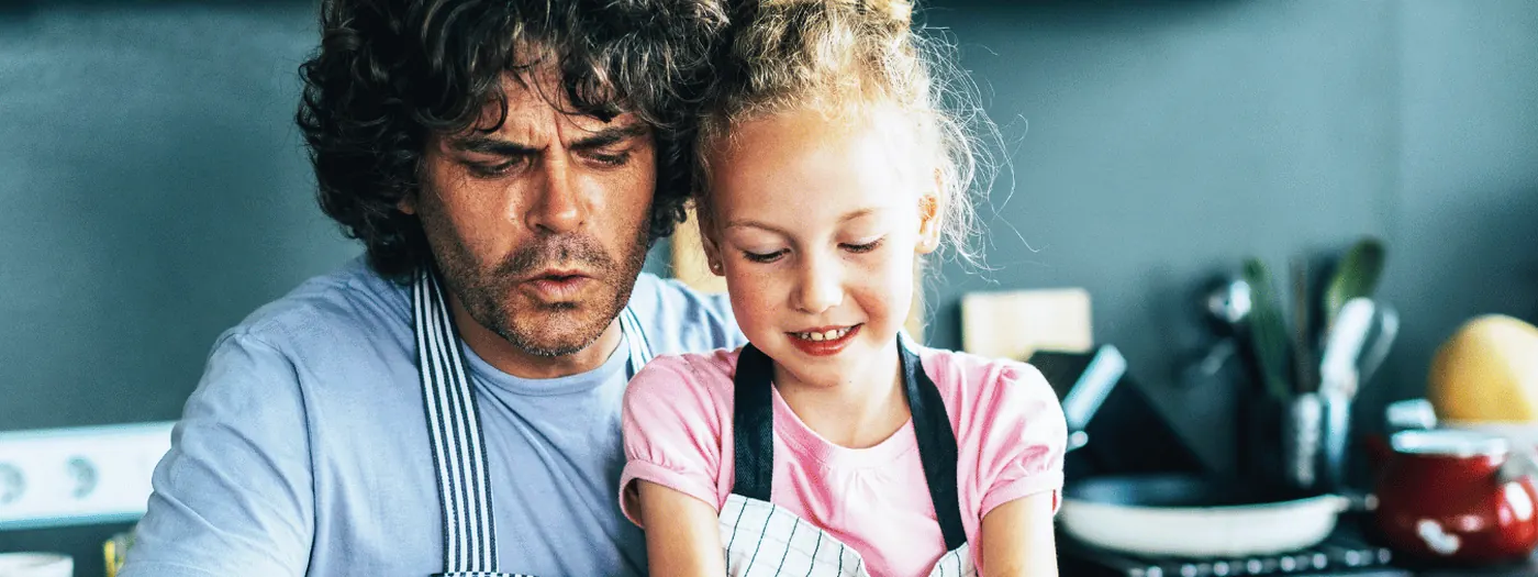 A father and daughter chopping vegetables together in a dark kitchen