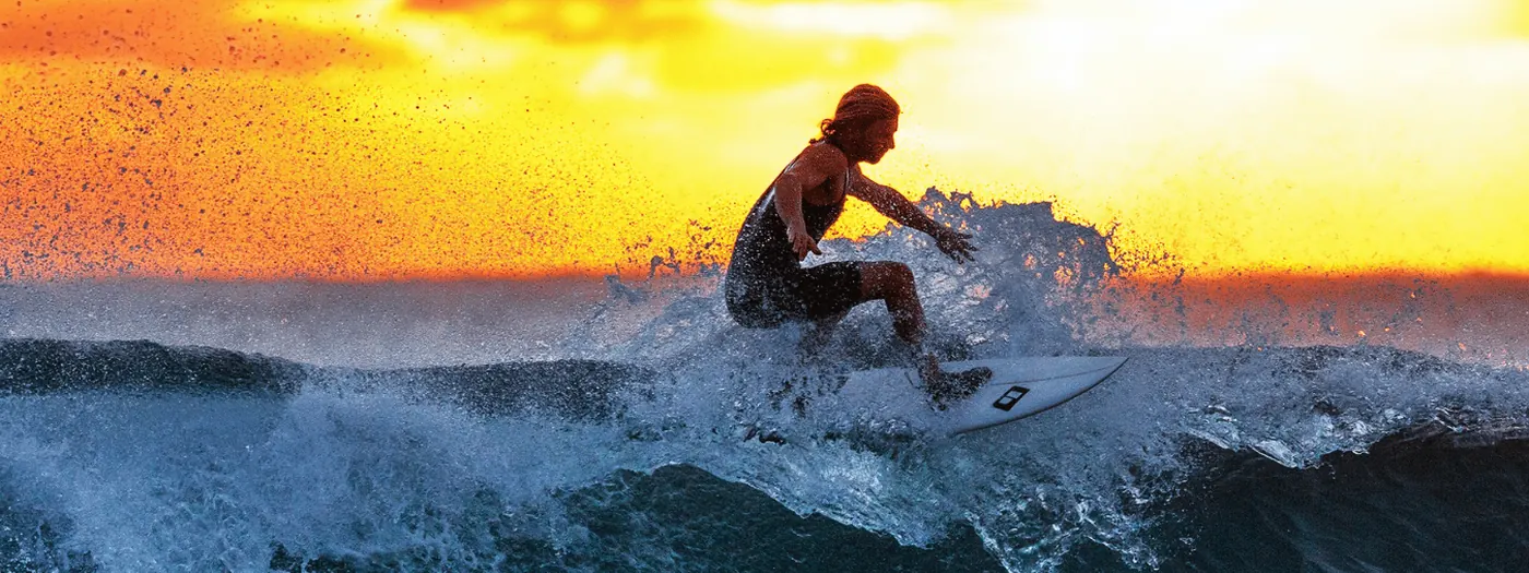 A surfer turning off the top of a wave at sunset