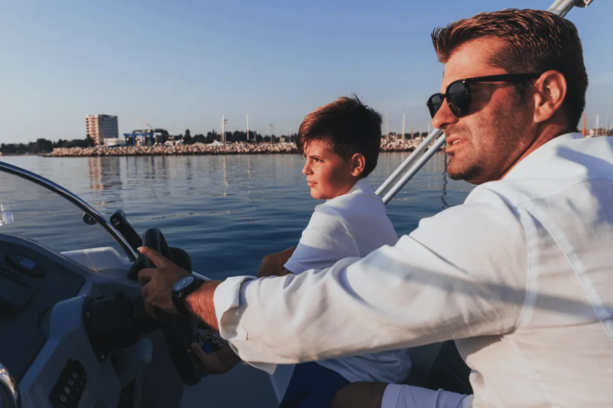 A father and son at the helm of a boat on open water