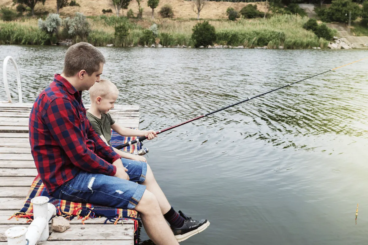 A father and son sitting on a jetty with rods out over the water