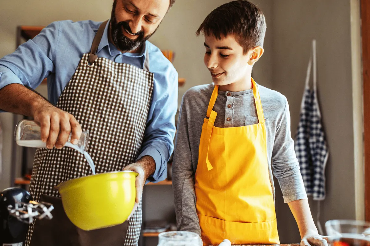 A father and son in aprons mixing a batter in a kitchen