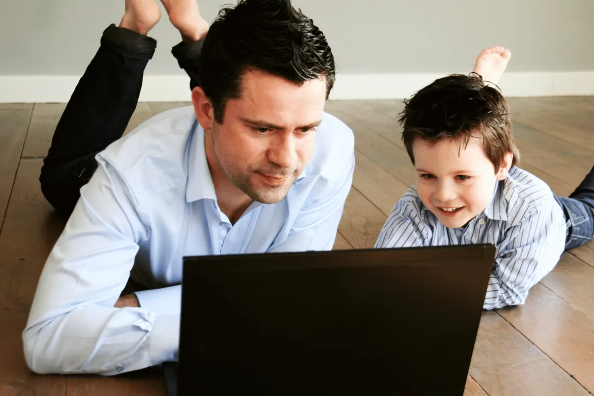 A father and son lying on the floor looking at a laptop together
