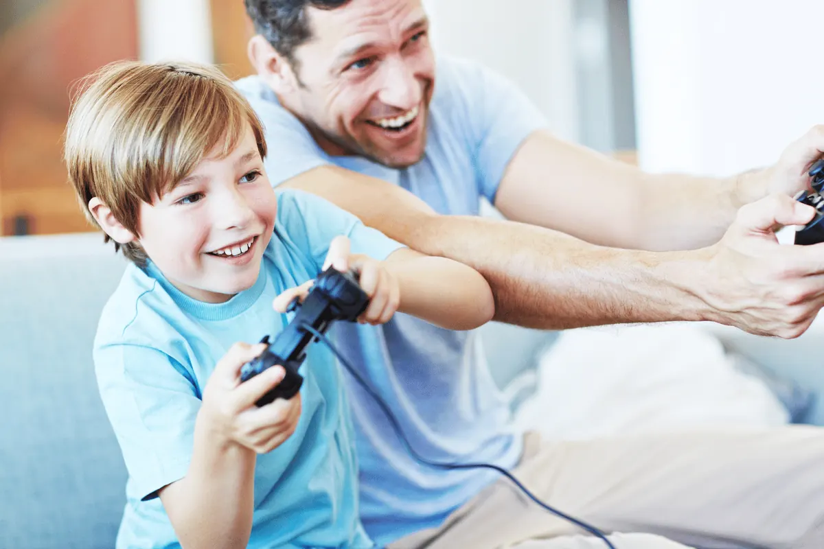 A father and his young son laughing on the couch, each holding a game controller