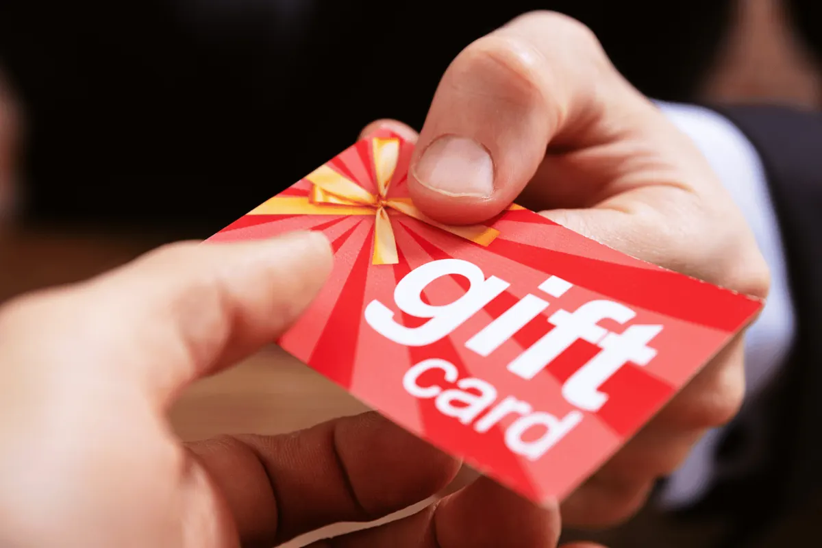 A hand passing a red gift card tied with ribbon
