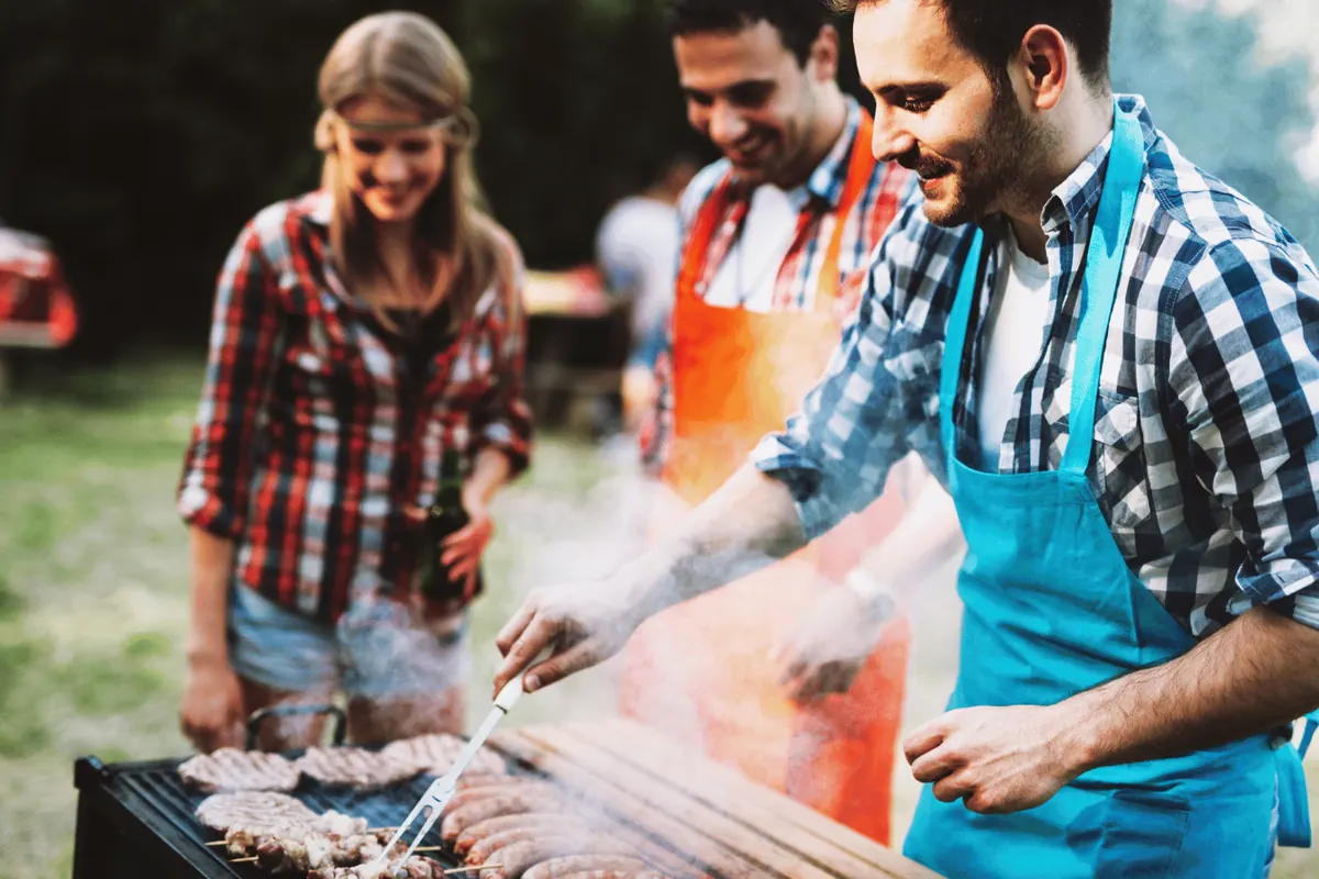 Three friends in aprons cooking over a barbecue in the smoke