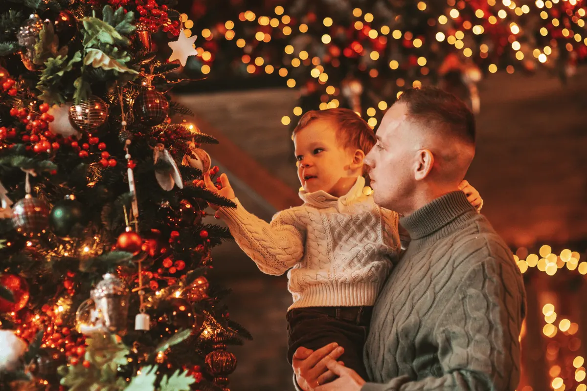A father holding his baby up to the lights on a Christmas tree