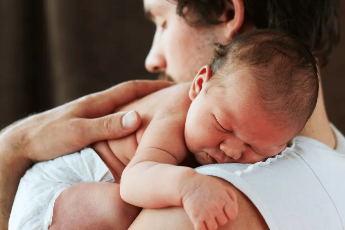 A newborn curled asleep in his father’s forearms