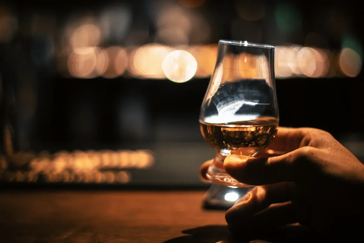 A hand holding a nosing glass of whisky in a dimly lit bar