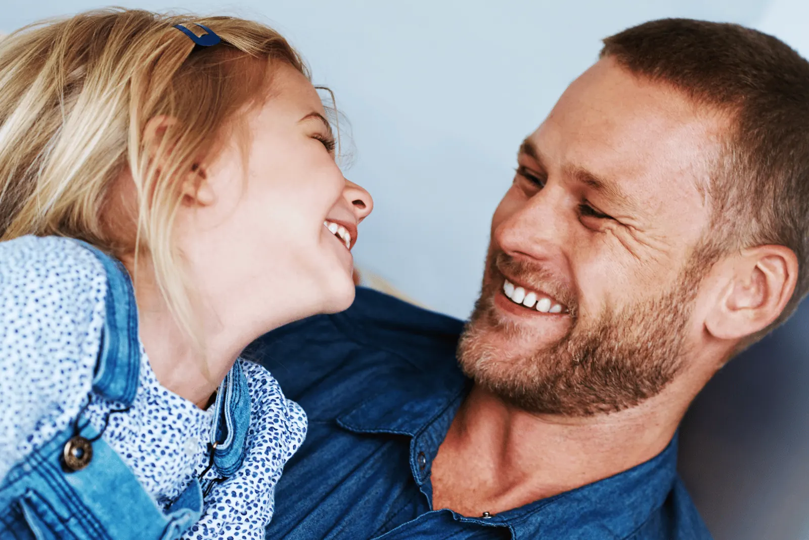 A father and his young daughter laughing together, foreheads close