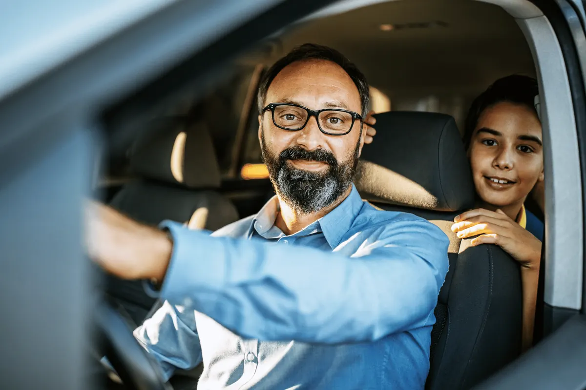 A father at the wheel with his son leaning through from the back seat
