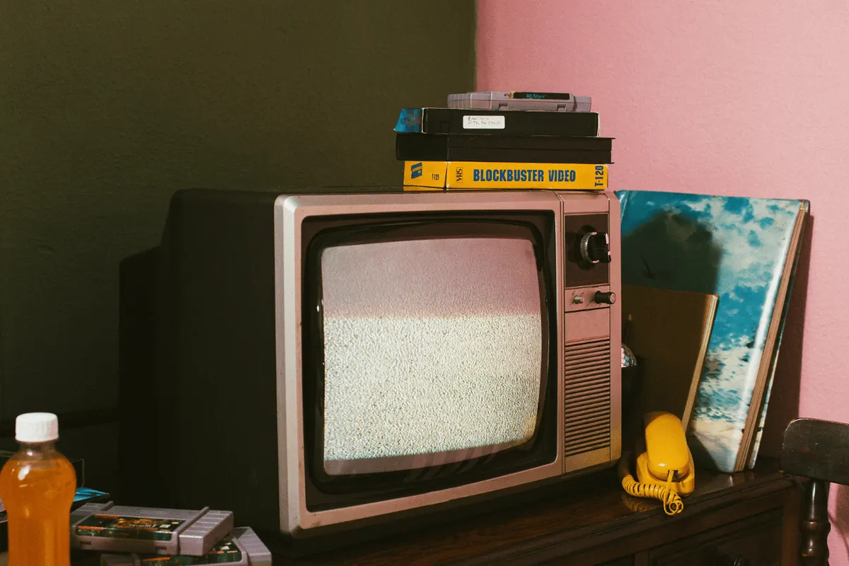 A wood-cased television on a sideboard beside records and a rental video tape