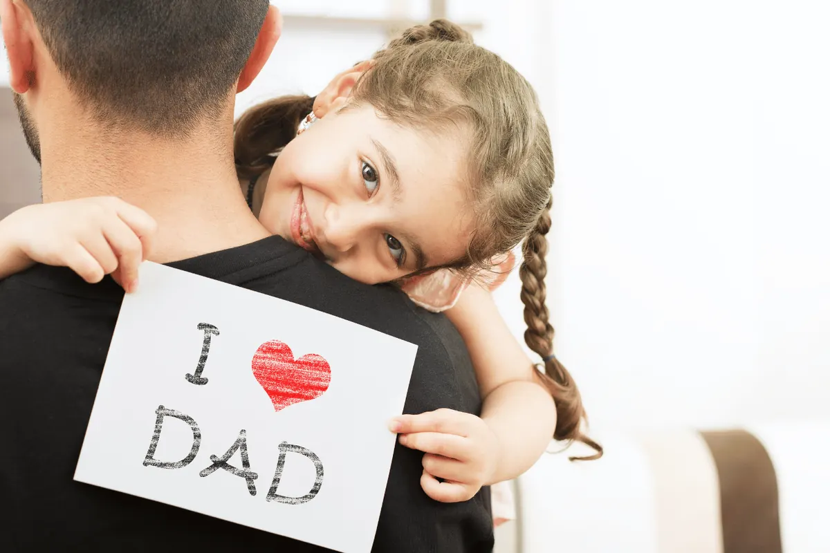 A girl hugging her father while holding up a hand-drawn I love Dad sign