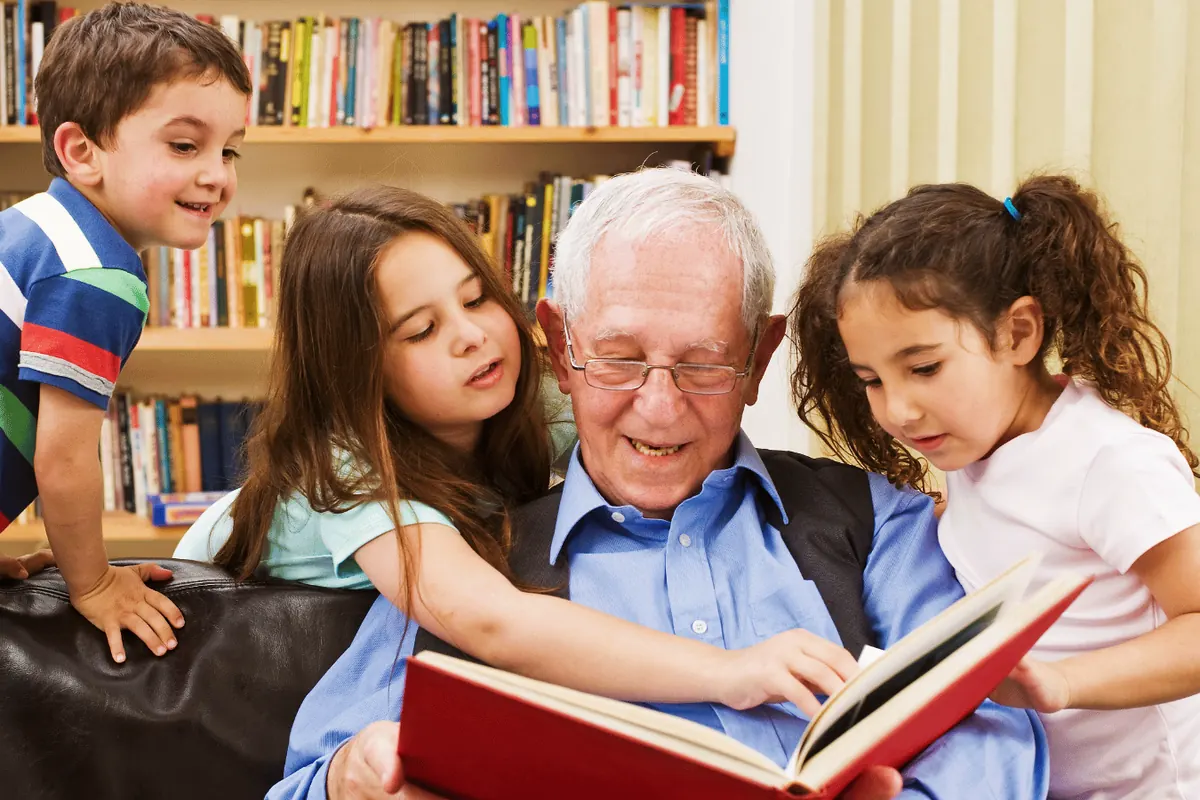 A grandfather reading a picture book to three grandchildren on the couch