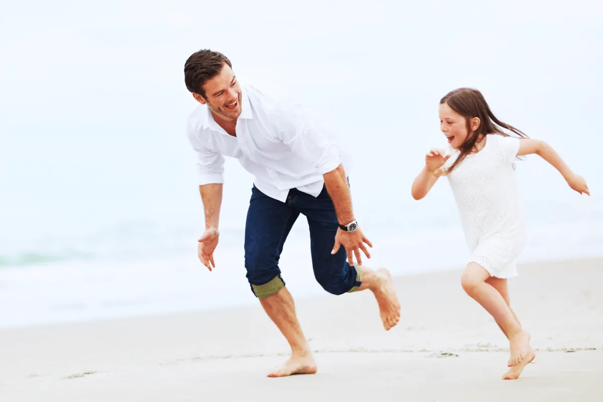 A father and daughter running barefoot along wet sand