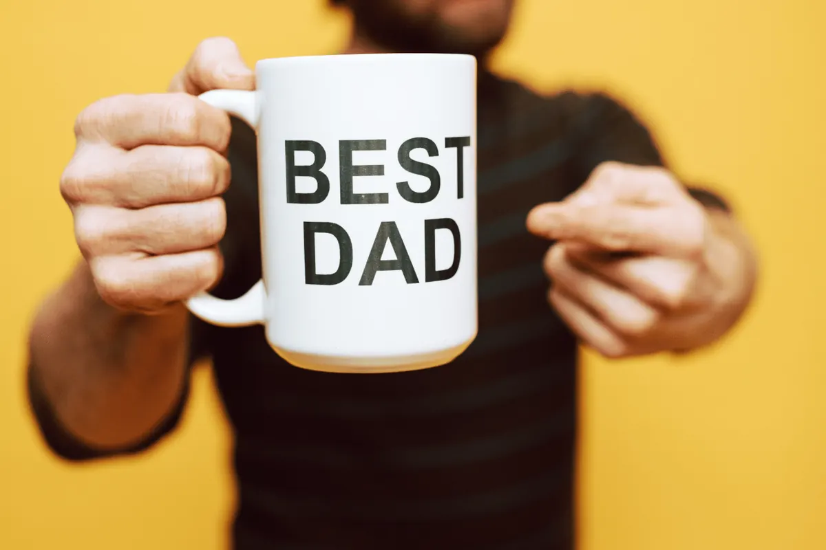 A man holding up a mug printed with the words Best Dad