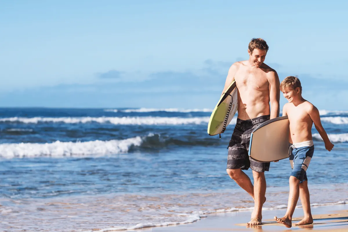 A father and son carrying boards down the beach towards the break