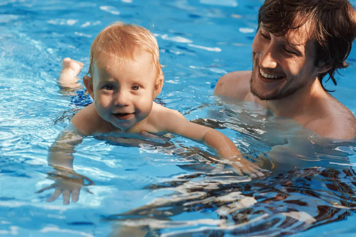 A father supporting his son as he swims across a pool