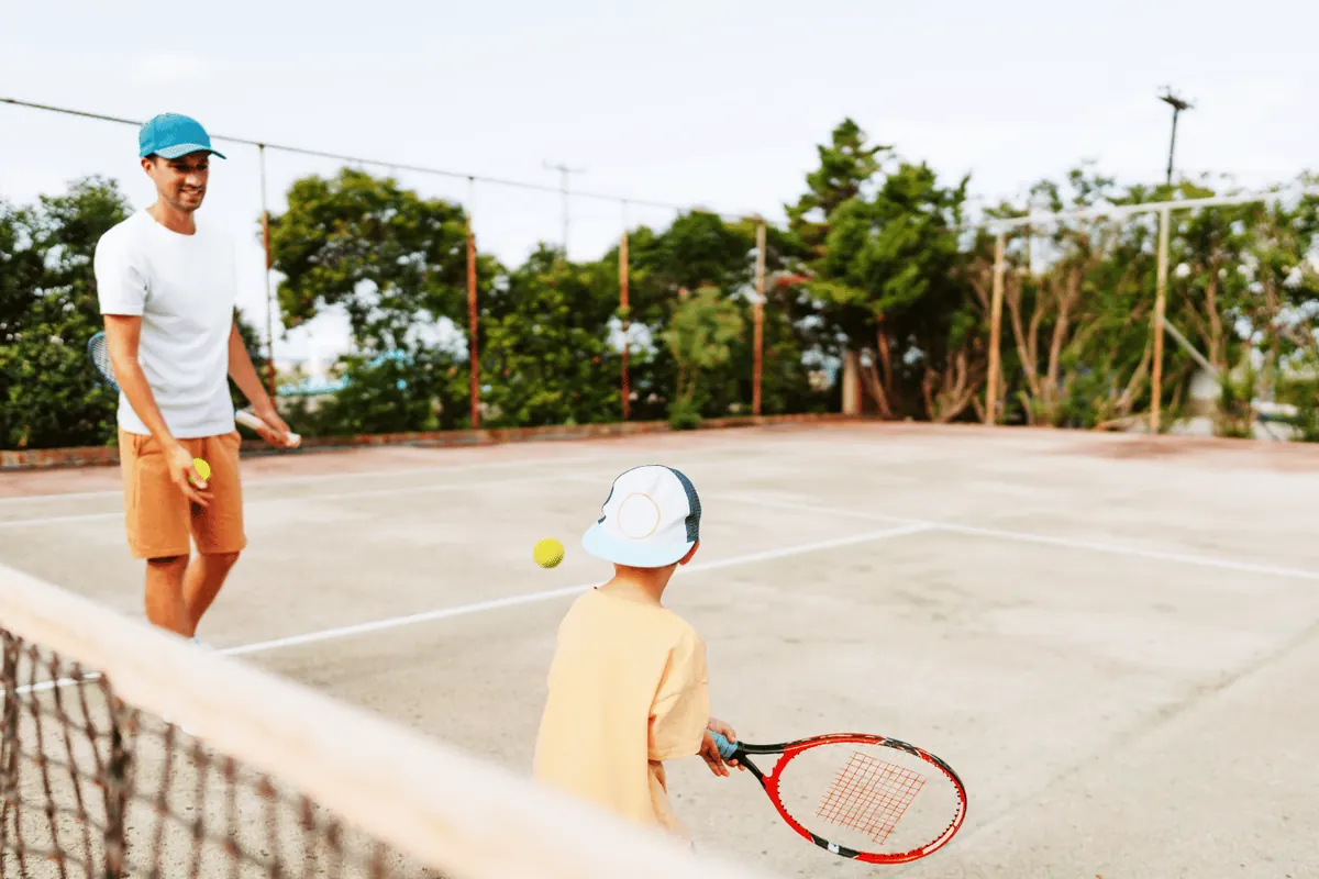 A father feeding balls to his son across a tennis net on a public court