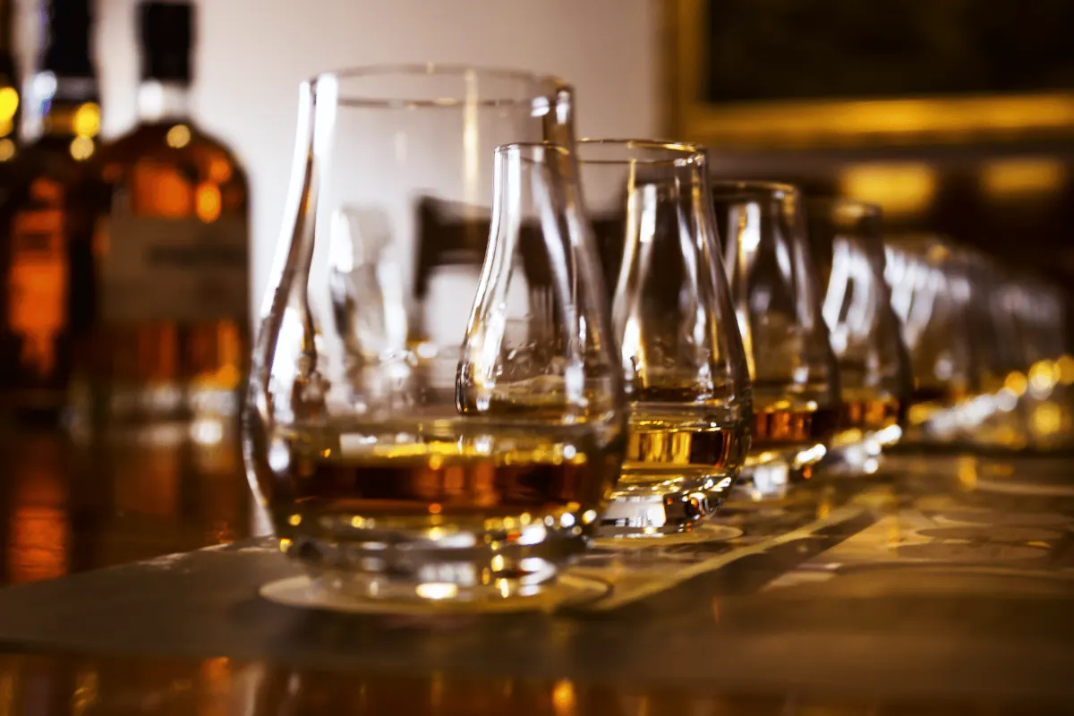 A row of nosing glasses poured for a whisky tasting, bottles behind